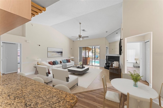 living room with ceiling fan, high vaulted ceiling, and light wood-type flooring