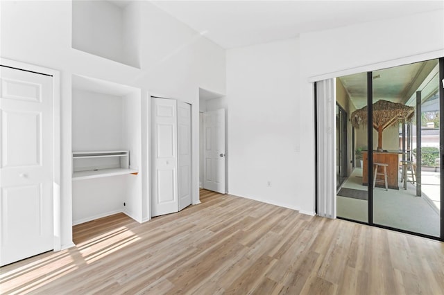 unfurnished bedroom with two closets, access to exterior, light hardwood / wood-style flooring, and a high ceiling