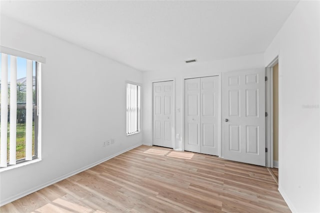 unfurnished bedroom with two closets and light wood-type flooring