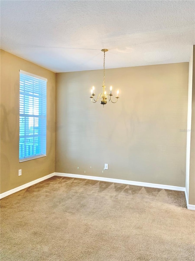 carpeted spare room featuring an inviting chandelier and a textured ceiling