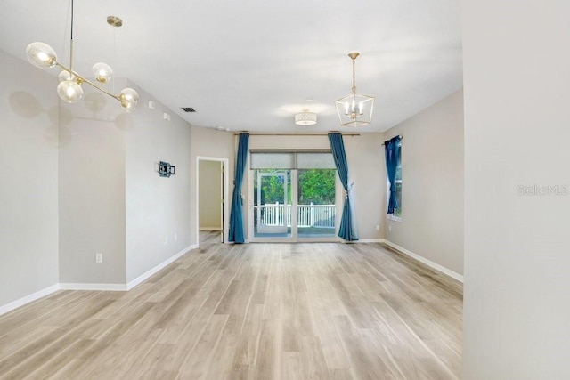 spare room with a notable chandelier and light wood-type flooring