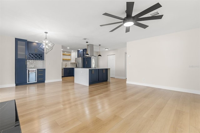 unfurnished living room with indoor bar, ceiling fan with notable chandelier, and light hardwood / wood-style floors