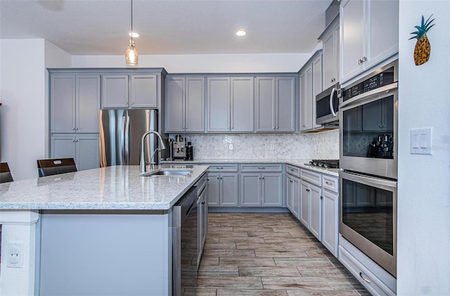 811 Winterside Dr, Apollo Beach, FL 33572 - kitchen featuring stainless steel appliances, gray cabinets, a kitchen island with sink, light stone countertops, and tasteful backsplash