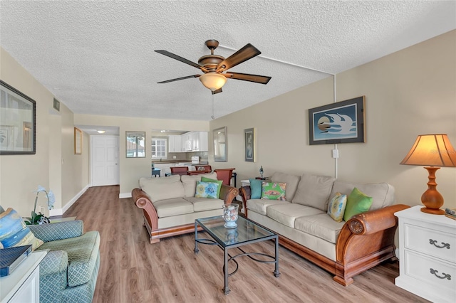 living room with ceiling fan, a textured ceiling, and light hardwood / wood-style floors