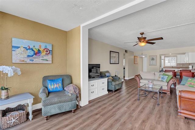 living room featuring ceiling fan, a textured ceiling, and light wood-type flooring