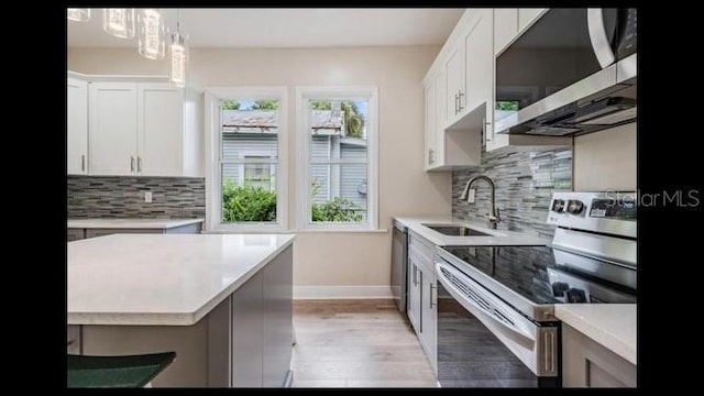 kitchen with pendant lighting, sink, white cabinets, stainless steel appliances, and light hardwood / wood-style flooring