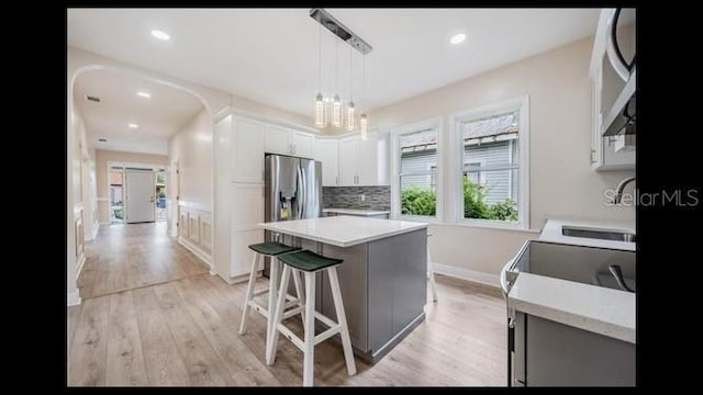 kitchen featuring white cabinetry, backsplash, a center island, light hardwood / wood-style floors, and decorative light fixtures