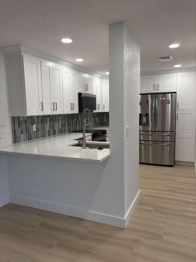 kitchen with white cabinetry, appliances with stainless steel finishes, backsplash, and light wood-type flooring