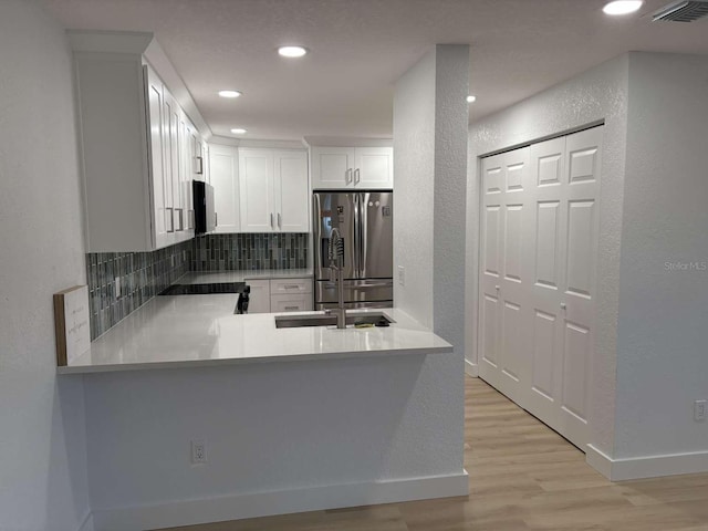 kitchen with white cabinetry, backsplash, stainless steel fridge, kitchen peninsula, and light wood-type flooring