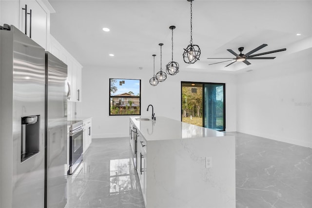 kitchen featuring appliances with stainless steel finishes, pendant lighting, white cabinetry, sink, and a kitchen island with sink