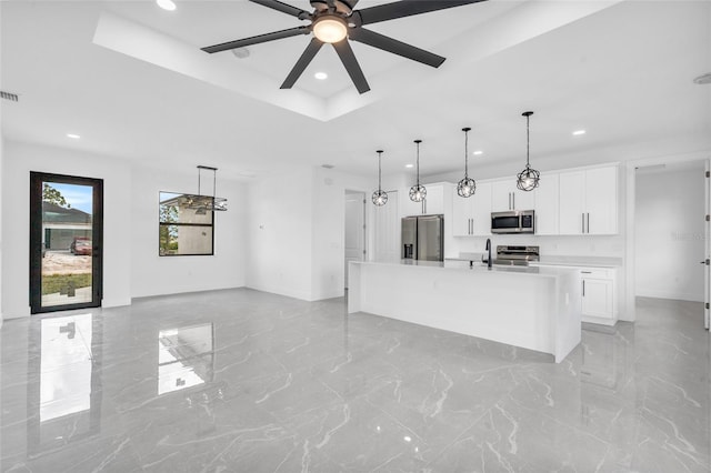 kitchen with a raised ceiling, white cabinetry, hanging light fixtures, stainless steel appliances, and a center island with sink