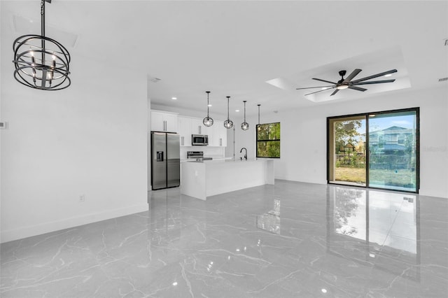 unfurnished living room featuring ceiling fan with notable chandelier, a tray ceiling, and sink