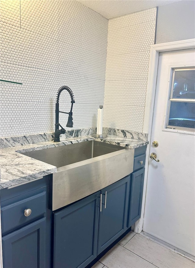 kitchen with sink, light stone countertops, a textured ceiling, and blue cabinetry