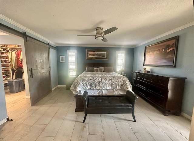 bedroom featuring crown molding, a walk in closet, a textured ceiling, a barn door, and light hardwood / wood-style floors