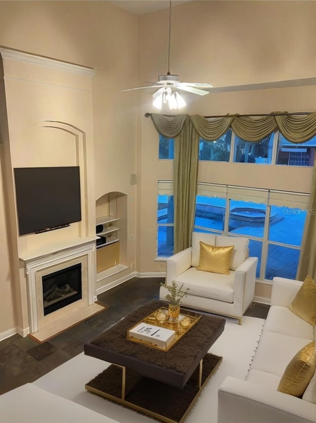 living room featuring a towering ceiling, built in features, a fireplace, ceiling fan, and dark wood-type flooring