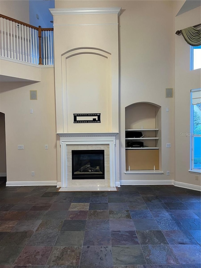 unfurnished living room featuring a premium fireplace, a towering ceiling, and built in features