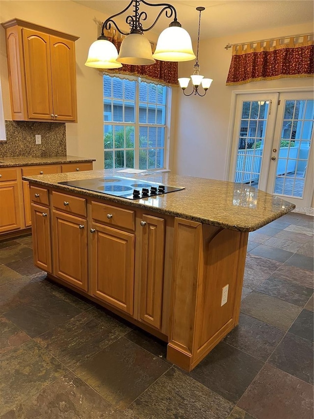 kitchen featuring tasteful backsplash, hanging light fixtures, black electric cooktop, a notable chandelier, and light stone countertops