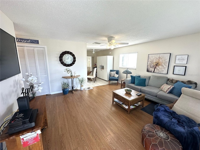 living area featuring a ceiling fan, a textured ceiling, baseboards, and wood finished floors