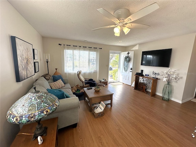 living area with ceiling fan, a textured ceiling, baseboards, and wood finished floors