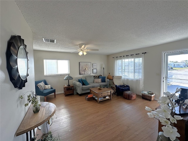 living room featuring a textured ceiling, ceiling fan, wood finished floors, visible vents, and baseboards