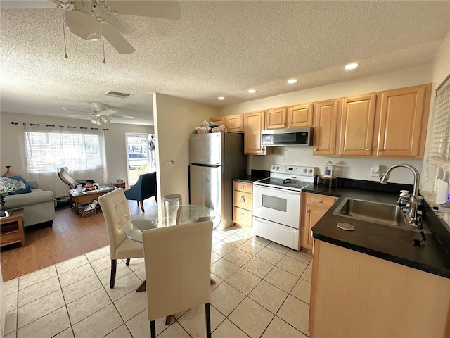 kitchen with light tile patterned floors, stainless steel appliances, dark countertops, light brown cabinetry, and a sink