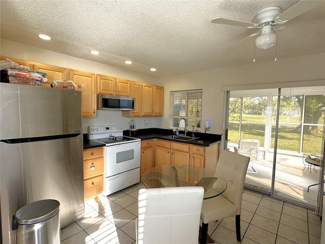 kitchen featuring stainless steel appliances, dark countertops, light tile patterned flooring, a sink, and a textured ceiling