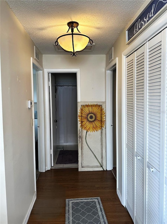 corridor with a textured ceiling, wood finished floors, visible vents, and baseboards