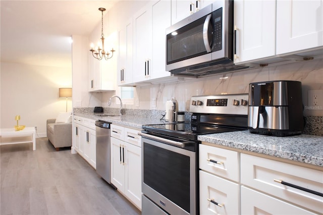 kitchen with light stone counters, appliances with stainless steel finishes, white cabinets, and a sink