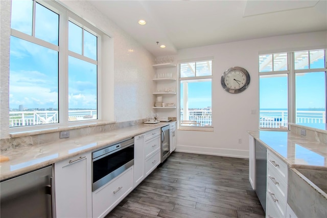 kitchen featuring light stone counters, a water view, appliances with stainless steel finishes, a healthy amount of sunlight, and white cabinets