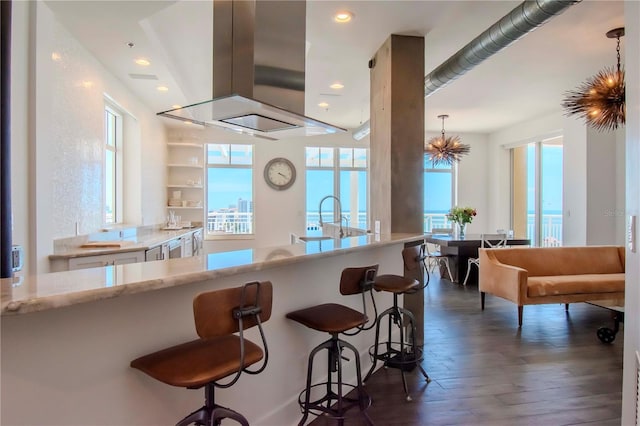 kitchen with a breakfast bar, island range hood, decorative light fixtures, and dark hardwood / wood-style flooring