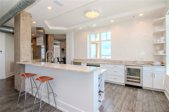 kitchen featuring light hardwood / wood-style flooring, white cabinetry, wine cooler, kitchen peninsula, and wall chimney exhaust hood