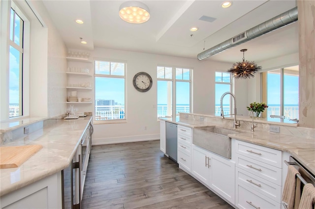 kitchen featuring sink, light stone counters, hanging light fixtures, stainless steel dishwasher, and white cabinets