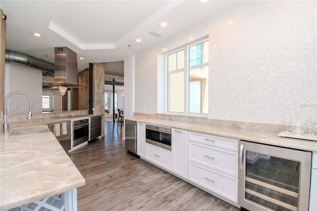 kitchen with wine cooler, sink, white cabinetry, stainless steel oven, and island exhaust hood