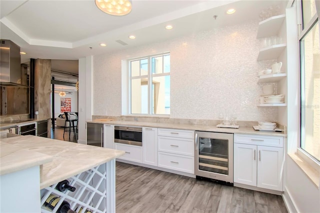 kitchen with white cabinetry, wine cooler, light stone countertops, light wood-type flooring, and wall chimney exhaust hood