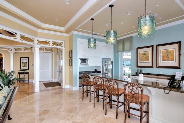 kitchen featuring appliances with stainless steel finishes, a breakfast bar, white cabinetry, dark stone countertops, and hanging light fixtures