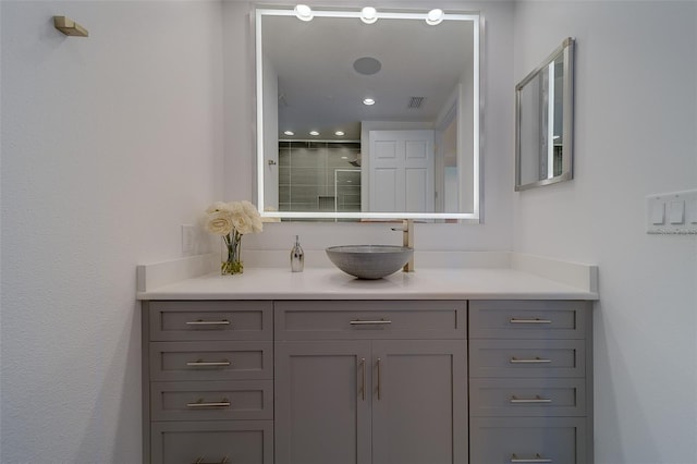 full bathroom with visible vents, a tile shower, and vanity