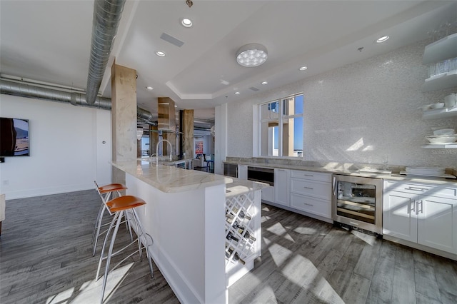 kitchen with wine cooler, wood finished floors, white cabinetry, and tasteful backsplash