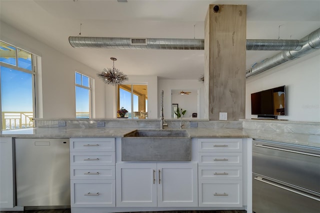 kitchen with visible vents, a peninsula, light stone countertops, white cabinetry, and a sink