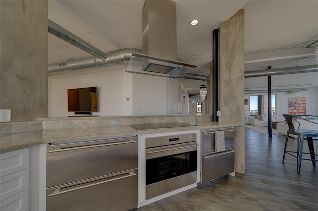 kitchen featuring dark wood-style flooring, light stone countertops, island exhaust hood, black electric stovetop, and stainless steel oven