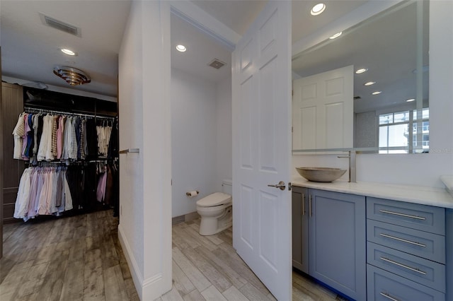 full bath with toilet, wood finished floors, vanity, visible vents, and a spacious closet