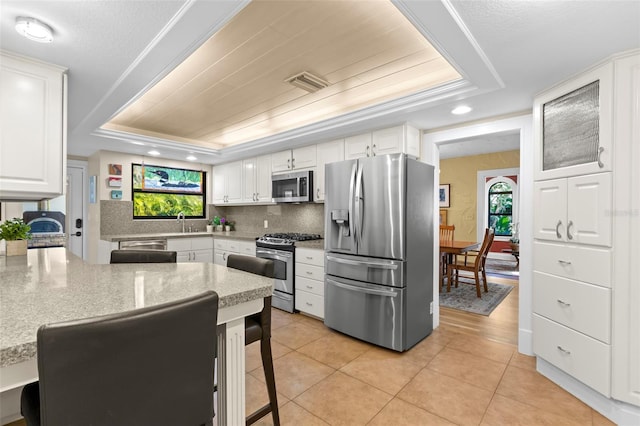 kitchen featuring appliances with stainless steel finishes, white cabinetry, light stone counters, a wealth of natural light, and a raised ceiling