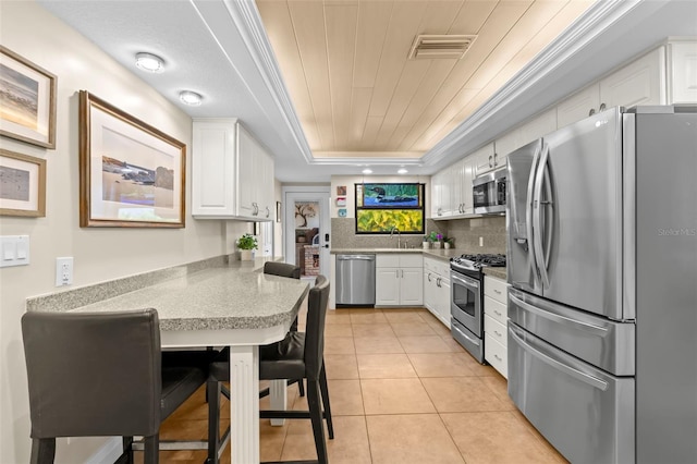 kitchen featuring appliances with stainless steel finishes, light tile patterned floors, white cabinets, and a tray ceiling