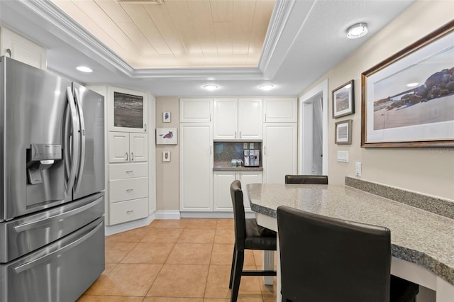 kitchen with light tile patterned flooring, white cabinetry, ornamental molding, stainless steel fridge, and a raised ceiling