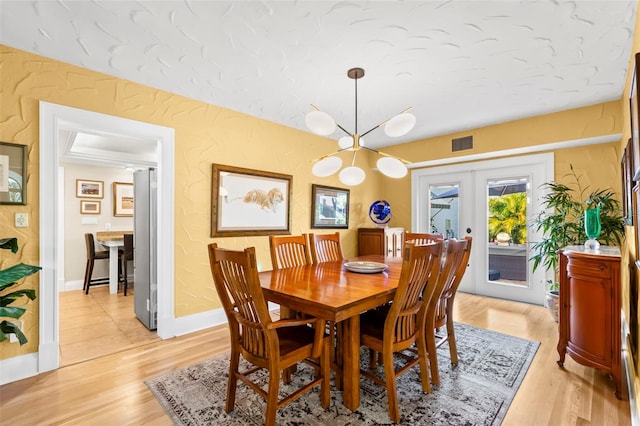 dining space featuring an inviting chandelier, light hardwood / wood-style floors, and french doors