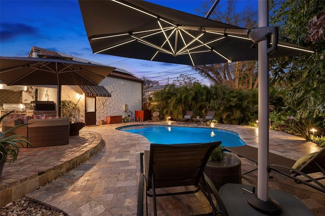 pool at dusk with an outdoor hangout area, a patio, and an outdoor kitchen