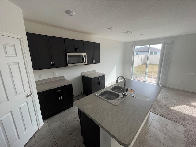 kitchen featuring light carpet, sink, a center island with sink, and a textured ceiling