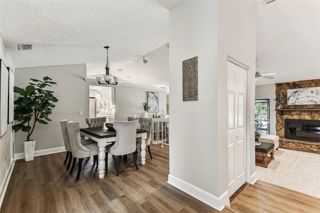 dining space featuring wood-type flooring, lofted ceiling, a textured ceiling, and a fireplace