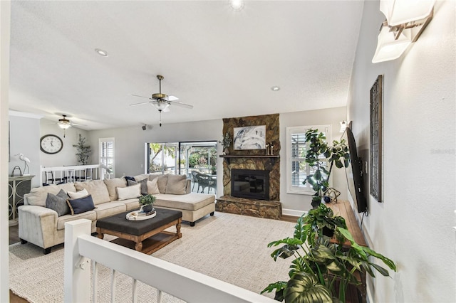 living room featuring ceiling fan, a stone fireplace, wood-type flooring, and a textured ceiling