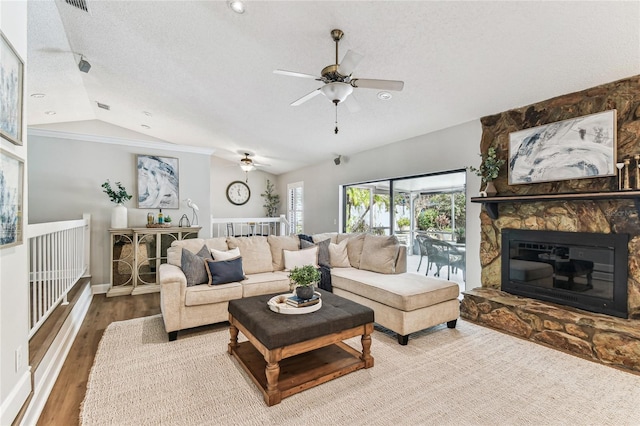 living room featuring a stone fireplace, wood-type flooring, vaulted ceiling, a textured ceiling, and ceiling fan