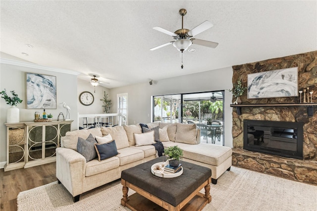 living room with wood-type flooring, a stone fireplace, ceiling fan, and a textured ceiling